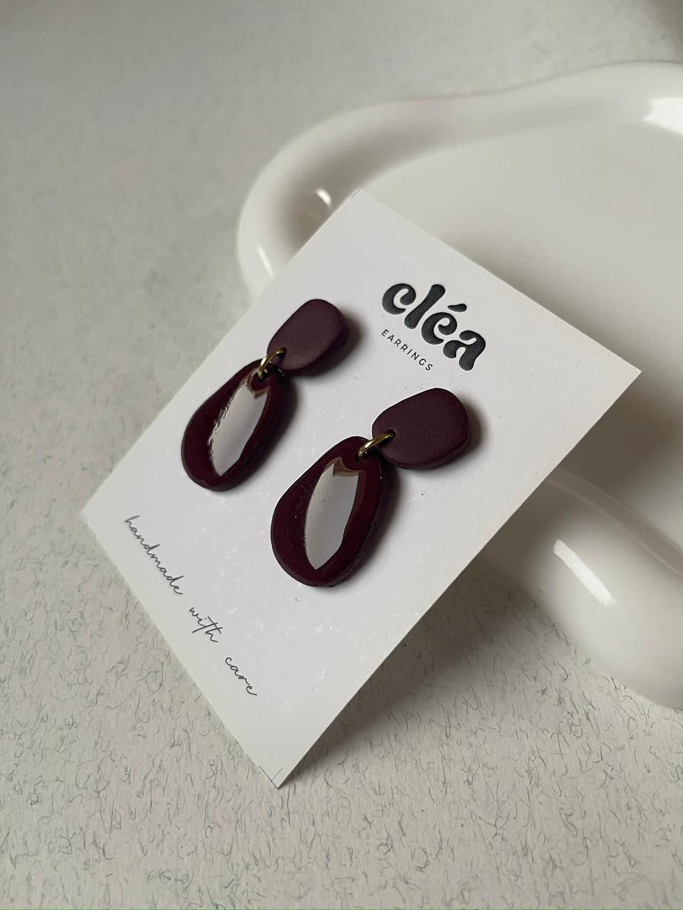 Pair of maroon earrings on a 'cleá' branded card against a white background