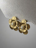 Gold flower-shaped earrings with pearl centers on a textured gray background