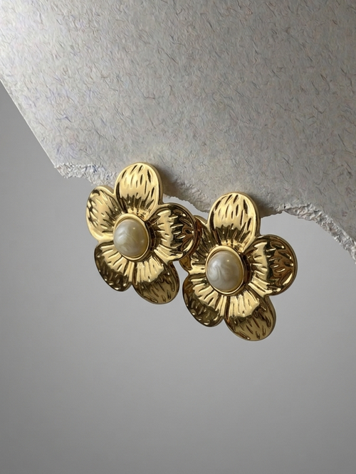 Gold flower-shaped earrings with pearl centers on a textured gray background