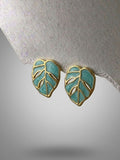 Teal leaf-shaped earrings with gold outlines on a light gray background