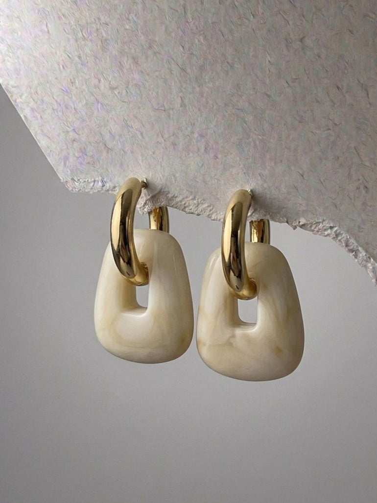 Pair of gold and beige hoop earrings on a textured surface