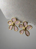 Pair of gold and pink flower-shaped earrings on a textured surface