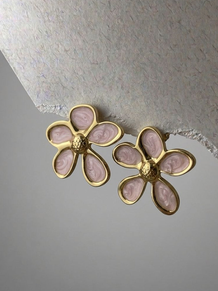 Pair of gold and pink flower-shaped earrings on a textured surface