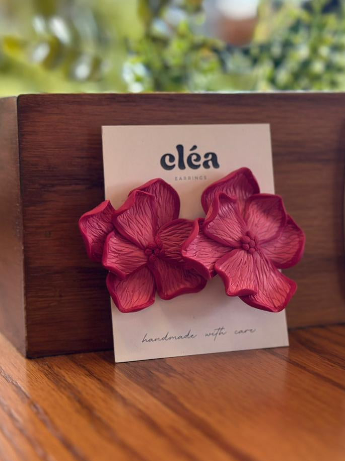 Fushia flower-shape handmade  earring on a card with 'Cleá' branding, placed on a wooden surface. 