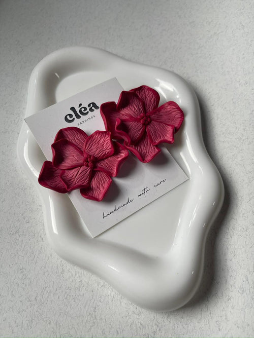 Red floral earrings on a white dish with 'clea' brand card on a gray background