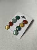 Colorful hexagonal earrings handmade earth tone on a 'cléa' branded card against a wooden background.